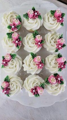 cupcakes with white frosting and pink flowers are arranged in a square tray