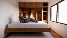 two men sitting on top of a bed in a room with bookshelves and shelves