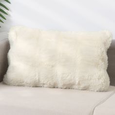 a white fur pillow sitting on top of a couch next to a green palm tree