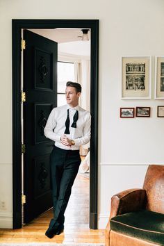 a man in a white shirt and black tie walking into a room with a chair