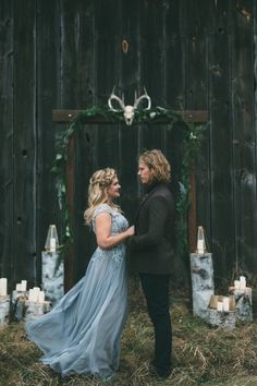 two women standing next to each other in front of a wooden wall with candles and deer heads