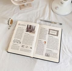 an open book sitting on top of a white bed next to a cup and pen