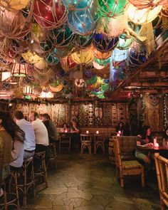 people sitting at tables in a restaurant with many lights hanging from the ceiling above them