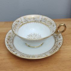 an antique tea cup and saucer set on a wooden table with gold trimmings