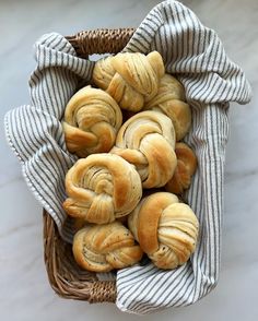 a basket filled with rolls sitting on top of a white marble counter next to a blue and white striped towel