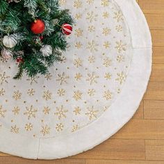 a christmas tree skirt on top of a wooden floor with ornaments and balls around it