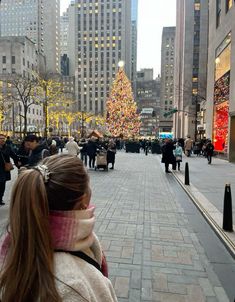 a woman wearing a scarf looking at a christmas tree in the middle of a city