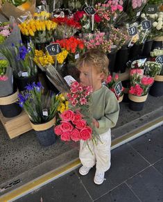 a little boy standing in front of a flower shop holding onto some pink and yellow flowers