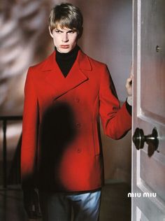 a woman in a red coat is standing by an open door and looking at the camera