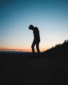 a man standing on top of a sandy beach next to the ocean at sunset with his hands in his pockets