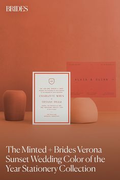 the wedding stationery is displayed in front of two vases and an orange wall