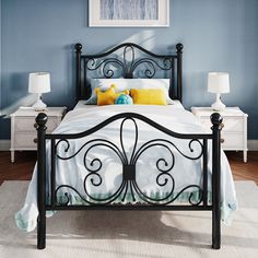 a bedroom with blue walls and black iron bed frame, white nightstands and yellow pillows