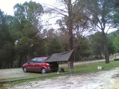 a red car parked next to a tent in the middle of a field with trees