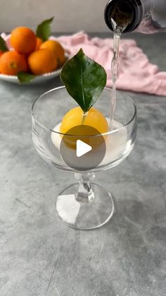 a glass bowl filled with oranges and water pouring from a bottle into the cup