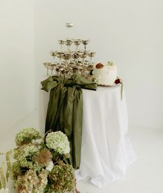 a table topped with a white cake and lots of greenery next to wine glasses