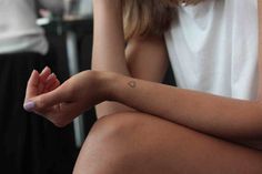 a woman with a small heart tattoo on her left arm sitting in front of a table