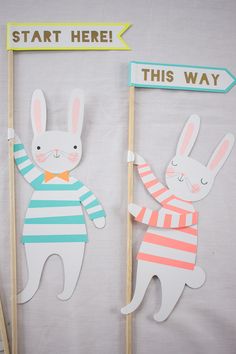 two paper rabbits holding up signs that say start here and this way on wooden sticks