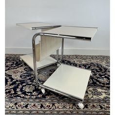 a chrome and glass side table on wheels with two open compartments sitting on top of it