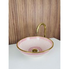 a pink and white bowl sink with gold faucet in the middle on a counter