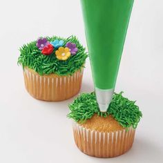 two cupcakes with green frosting and flowers on them, one has a plastic tube sticking out of it