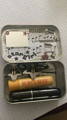 an open tin with music notes and pens in it on top of a piece of paper