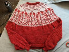 a red and white sweater sitting on top of a table next to some sewing supplies