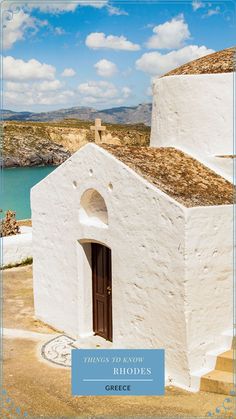 a white building with a brown door on the side and water in the back ground