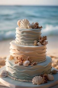 a three tiered cake with seashells on the top is sitting in the sand