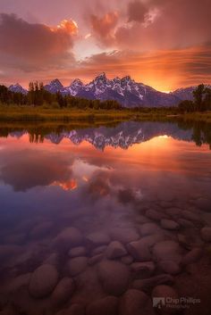 the sun is setting over a mountain range with rocks in the foreground and a body of water below it