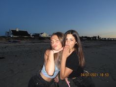 two young women sitting on the beach with their hands in their mouths and one is covering her mouth