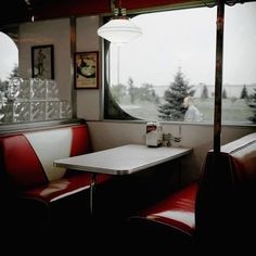 two booths with red leather seats and a white table in front of a large window