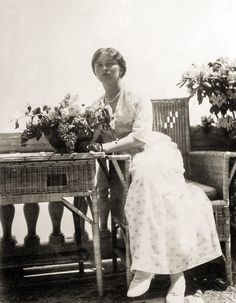 an old black and white photo of a woman sitting at a table with flowers on it