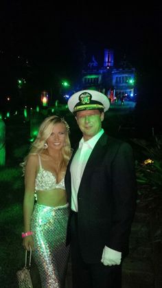 a man and woman dressed in costumes pose for a photo at night time, with the lights on behind them