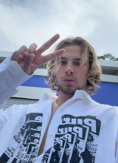 a man with long hair making the peace sign while standing in front of a building