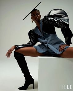 a woman sitting on top of a white block wearing black boots and a blue dress