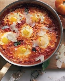 an egg dish in a pan on a cutting board next to some tomatoes and garlic