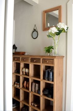 a vase with flowers on top of a wooden shelf next to a mirror and shoes