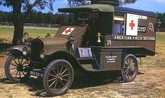 an old fashioned ambulance is parked in the grass near some trees and other items on display