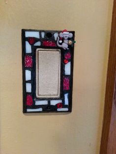 a white and black mosaic frame with a teddy bear sitting on top of it next to a yellow wall