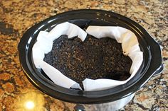 a black crock pot filled with dirt on top of a granite countertop next to a white paper towel