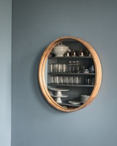 a round mirror hanging on the side of a wall next to a shelf filled with dishes