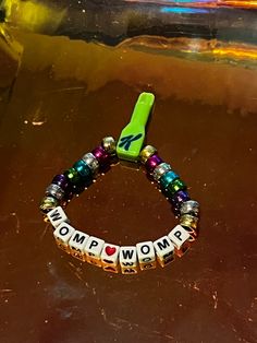 a bracelet with the word wowm spelled on it and a green phone charm attached to it