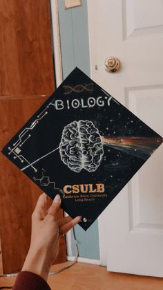 a person holding up a black graduation cap with a brain on it