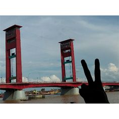 a person's hand is up in front of two red bridge towers with one pointing at the camera