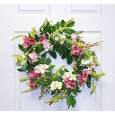 a wreath with pink and white flowers is hanging on a front door, surrounded by greenery