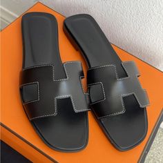 Brand New Hermes Calfskin Oran Sandals In Black 2 Dust Bag, Box Included Color Code : Black Made In Italy These Stylish Slippers Are Crafted Of Polished Smooth Box Calfskin Leather In Black With Insoles Of Leather. The Toe Strap Is A Cross Over Large Hermes H With White Stitching. Black Flat Heel Calf Leather Sandals, Luxury Black Sandals With Leather Lining, Designer Black Leather Sandals, Classic Black Flat Heel Sandals, Black Designer Leather Sandals, Black Sandals With Leather Lining For Evening, Luxury Black Sandals With Leather Sole, Designer Black Sandals With Leather Sole, Luxury Black Flat Heel Sandals