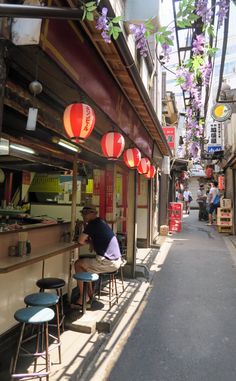 a man sitting at a table in front of a restaurant with lanterns hanging from the ceiling