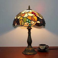 a stained glass lamp sitting on top of a wooden table next to a coffee cup