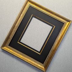 a gold frame with a white square in the middle on a gray wall behind it