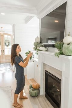 a woman standing in front of a fireplace with pumpkins on the mantel next to her